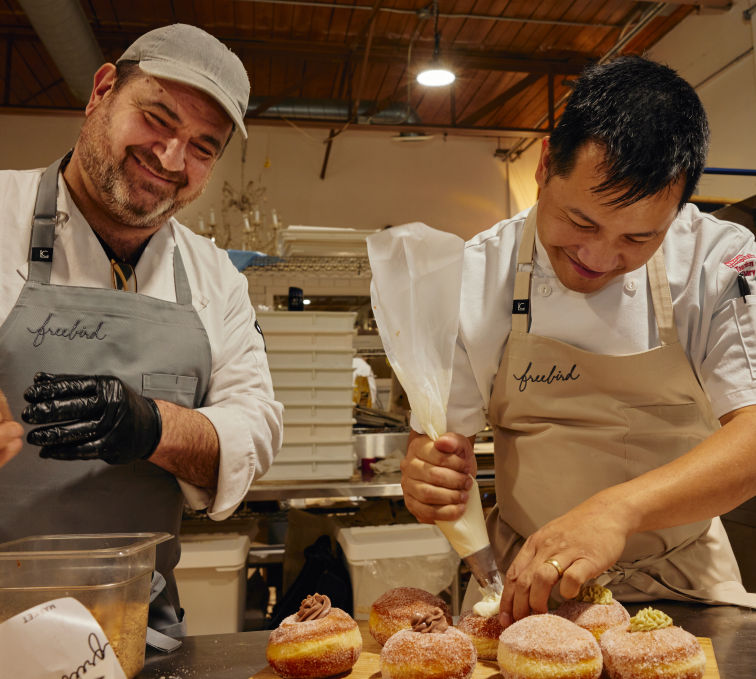 Two freebird pastry chefs, smiling and adding finishing touches to pastries